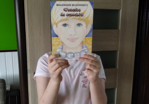 Praca Wiktorii Filipczak: Zdjęcie przedstawia dziewczynę w białej bluzkę. Twarz zastąpiono okładką książki „Wnuczka do orzechów Małgorzaty Musierowicz.